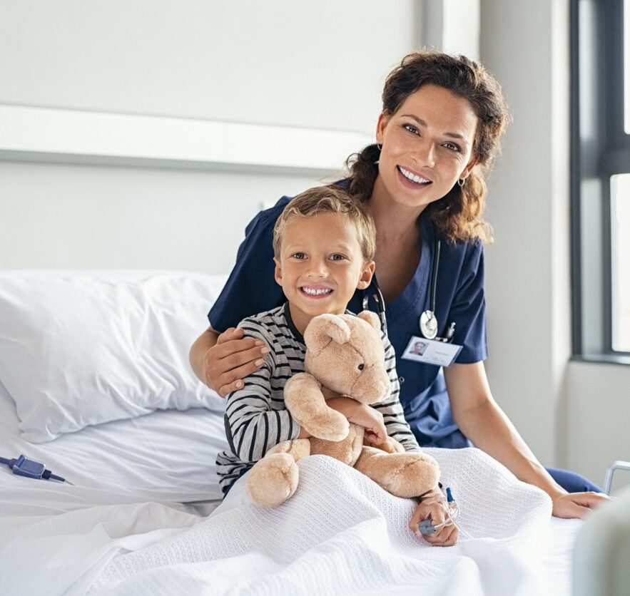 Glückliche Krankenschwester auf der Kinderstation mit Jungen mit Teddybär, die in die Kamera schauen.